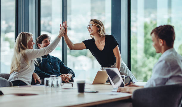 website traffic success - Female professional giving a high five to her colleague in conference room. Group of colleagues celebrating success in a meeting.